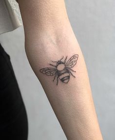 a woman's arm with a small tattoo of a bee on the back of it