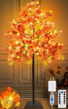 a lighted tree with orange leaves on it and remote controls in front of the wall