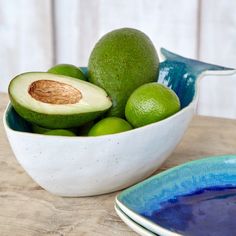 a bowl filled with limes and an avocado on top of a wooden table