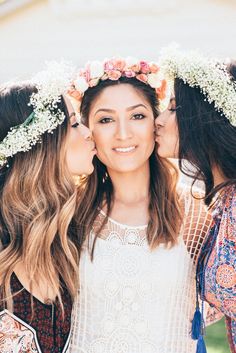 three women with flower crowns on their heads and one woman kissing the other's cheek