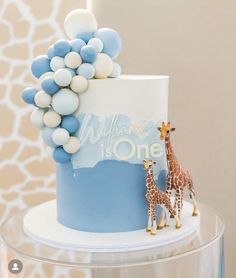 a blue and white cake with two giraffes on the top, and balloons in the middle