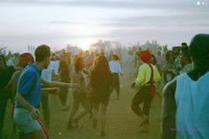 a group of people standing around each other on a field with the sun setting in the background