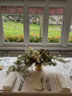 the table is set with silverware and flowers in front of two large windows that look out onto a lush green field