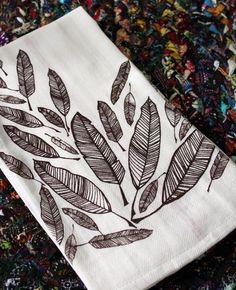 a white towel with black leaves on it sitting on a colorful cloth covered tablecloth