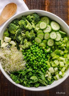 a bowl filled with green vegetables on top of a wooden table next to a spoon