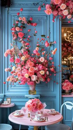 a table with pink flowers on it in front of a blue paneled wall and chandelier