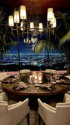 a dining room table set with place settings and candles in front of a city view