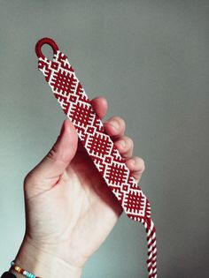 a hand holding up a red and white knitted tie with an ornament on it