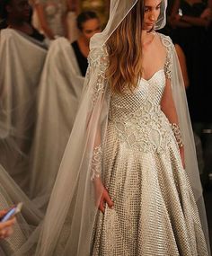 a woman in a wedding dress with a veil on her head walking down the runway