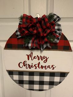 a merry christmas sign hanging on the front door with a red and black plaid bow