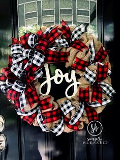 a wreath with the word joy is hanging on a black front door, decorated with red and white buffalo plaid ribbon