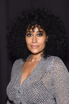 a woman with black hair wearing a silver dress and posing for the camera in front of a black background