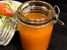 a glass jar filled with orange liquid next to a plate of salad on a table