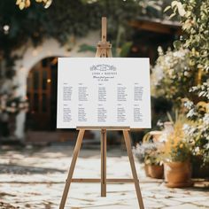 an easel with a wedding seating plan on it in front of some flowers and trees