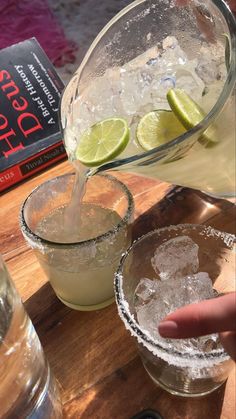 two glasses filled with ice and limes next to a book