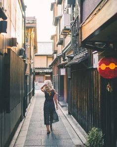 a woman is walking down an alleyway in the city with buildings on both sides