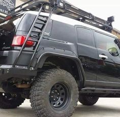 a large black truck parked in front of a building with a ladder on it's back