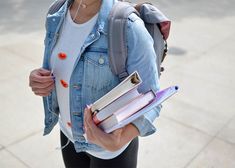 a woman holding two books in her hands and wearing headphones while walking down the street