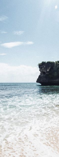 a person walking on the beach with a surfboard in their hand and an island in the background