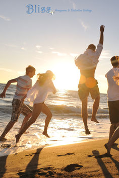 four people jumping up in the air on a beach near the ocean at sun set