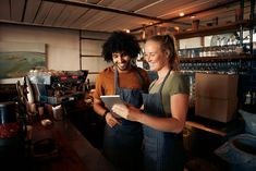 two people in aprons are looking at something on a tablet screen while standing next to each other