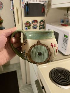 a person holding a mug in their hand next to a stove top oven with magnets on it