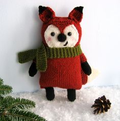 a knitted stuffed animal wearing a red sweater and green scarf next to a pine tree