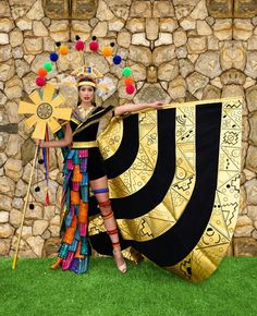 a woman in costume holding a large black and gold flag next to a stone wall