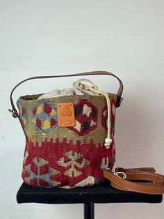 Unique kilim bucket bag from the "BEBEK" collection. Made with our best vintage kilims. It measures 20 cm in diameter and 18 cm high. The round leather handle with old gold metals measures 30 cm. The interior of the bag is closed in a tobacco bag and with a leather strap finished in two handmade glass balls. The bag has an optional handle (105 cm x 2 cm) that allows you to carry the bag as a crossbody or shoulder bag. They are light bags that are easy to carry. Our "BEBEK" kilim bags with their Weaving Bucket Bag For Travel, Bohemian Bucket Bag For Market, Daily Use Bucket Bag With Weaving, Traditional Bucket Bag With Leather Handles, Traditional Bucket Bag With Leather Handles For Daily Use, Traditional Bucket Bags With Leather Handles, Red Bohemian Bucket Bag, Kilim Bag, Glass Balls