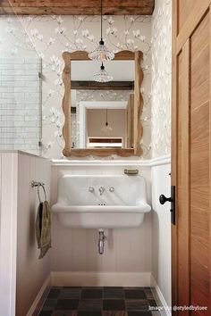 a white sink sitting under a mirror in a bathroom next to a wooden door and window