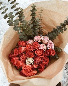 a bouquet of red and white roses in brown paper with eucalyptus leaves on the side