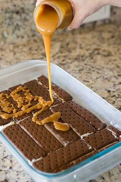 someone pouring peanut butter on top of a chocolate cake in a baking dish with graham crackers