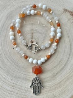 A pendant comprised of a silver plated Hamsa pendant and faceted Carnelian bead (2.5'' x 0.875'') is framed by shell, Fossil Jasper and dyed Quartz beads strung on 0.46 mm flexible wire. This necklace is 19.5'' in length with a silver plated toggle clasp. Nickel and Lead Free.  ------------------------------ All of my jewelry pieces come in a stylish drawstring pouch, ready to wear or gift! Items will ship within 1-3 business days after an order is placed and are always packed with care & love in a pet-friendly home.  **Note** Jewelry items are not waterproof, therefore it is suggested to remove prior to bathing, swimming, etc. -------------------------------- Thanks for viewing this item!  Please contact me with any questions!  I do custom orders! ~Rachel~ To see more handmade jewelry, yo White Gemstone Beads For Jewelry Making, Handmade White Beads Gems And Cabochons For Gifts, White Agate Beaded Necklace With Gemstone, White Polished Beads Gems And Cabochons For Gifts, Meditation Jewelry With Faceted Agate Beads, White Gemstone Pendant Beaded Necklace, White Agate Beaded Necklace For Gifts, Spiritual White Beaded Pendant Necklace, White Agate Gemstone Beaded Necklace