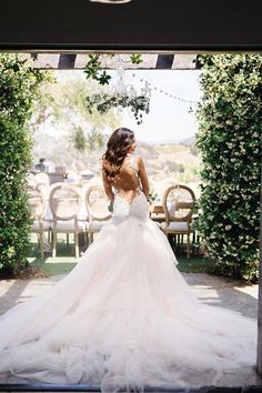 a woman in a wedding dress is looking out the window at an outdoor area with tables and chairs