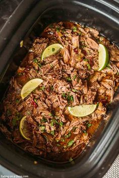 shredded pork in a slow cooker with limes and cilantro on the side