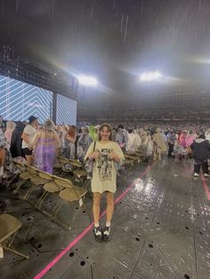 a woman standing in the rain at a stadium with lots of people sitting on chairs