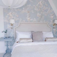 a white bed sitting in a bedroom next to a wallpaper covered with birds and flowers