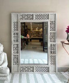 a white carved mirror sitting on top of a table next to a vase with flowers