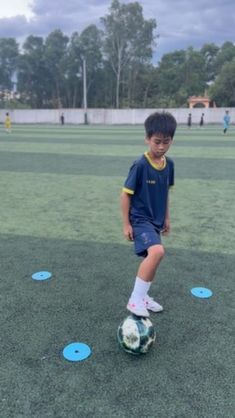 a young boy kicking a soccer ball on top of a green field with blue circles