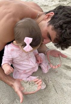 a man kissing a baby on the beach with sand in front of him and her