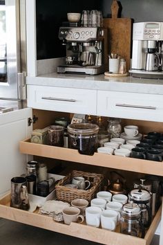 an open drawer in a kitchen filled with dishes and cups