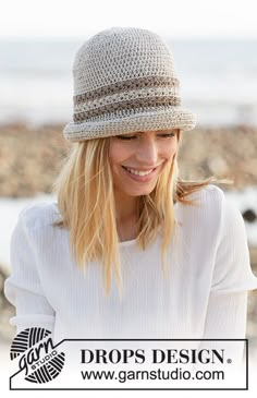 a woman wearing a white shirt and a beige hat smiles while standing on the beach