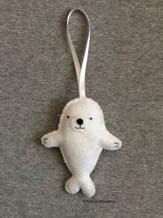 a white stuffed animal ornament hanging from a silver ribbon on a gray surface