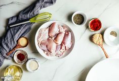 raw chicken in a white bowl surrounded by spices and seasonings on a marble counter top