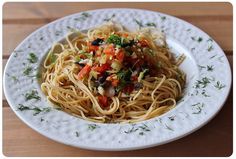 a white plate topped with pasta covered in sauce and toppings on top of a wooden table