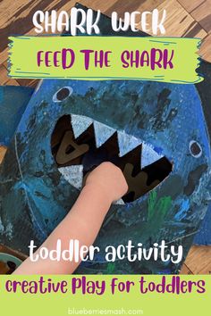 a toddler's hand holding a paper shark with the title shark week feed the shark