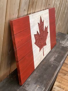 the canadian flag is painted on top of a wooden bench with wood slats behind it