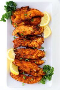 chicken wings with lemon wedges and parsley garnish on a white plate