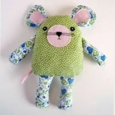 a green teddy bear with blue flowers on it's body and ears, sitting against a white wall