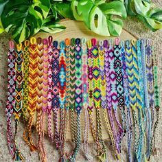 the colorful bracelets are lined up next to each other on the floor with green plants in the background